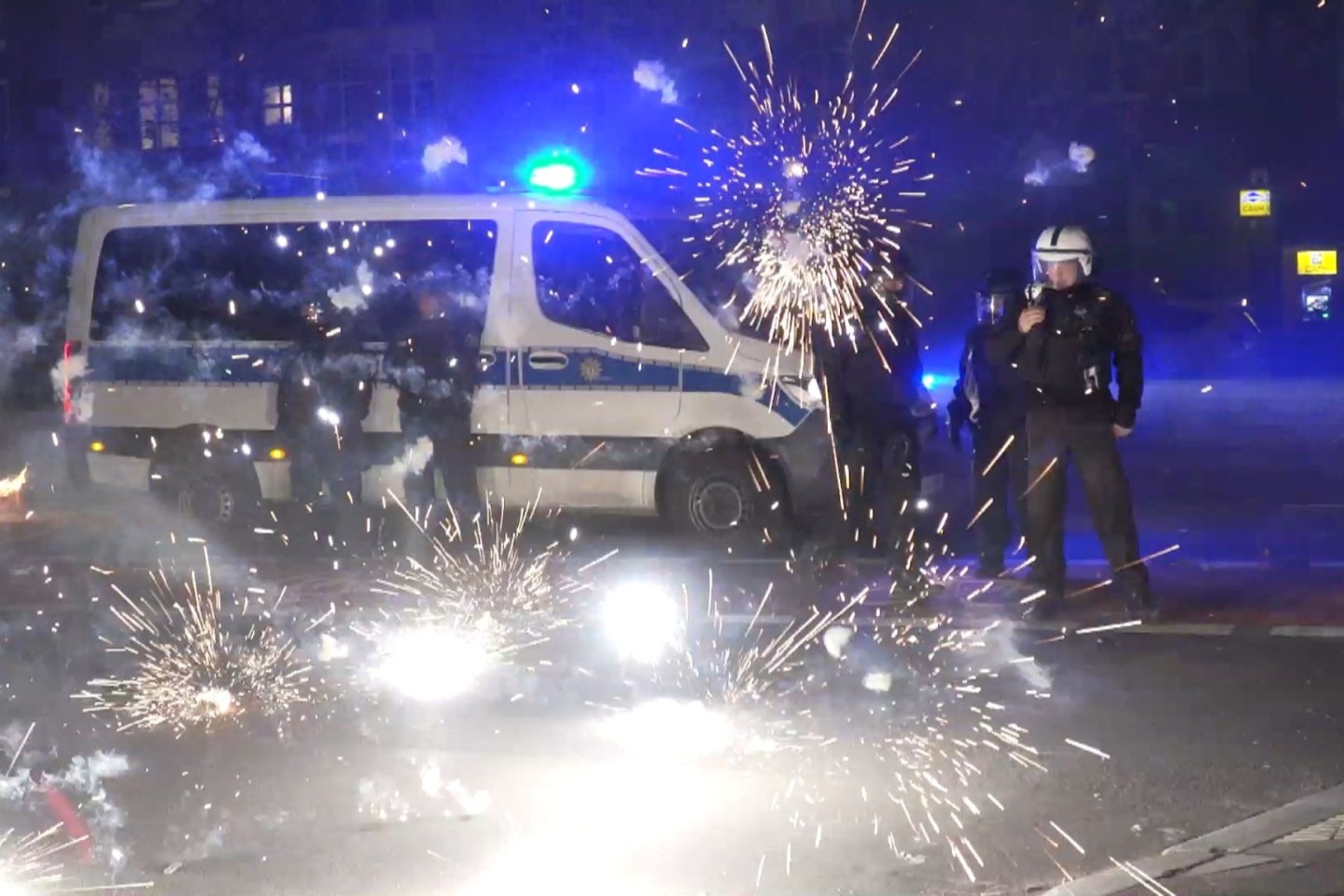 Polizeibeamte stehen in der Silvesternacht 2022 in Berlin hinter explodierendem Feuerwerk.