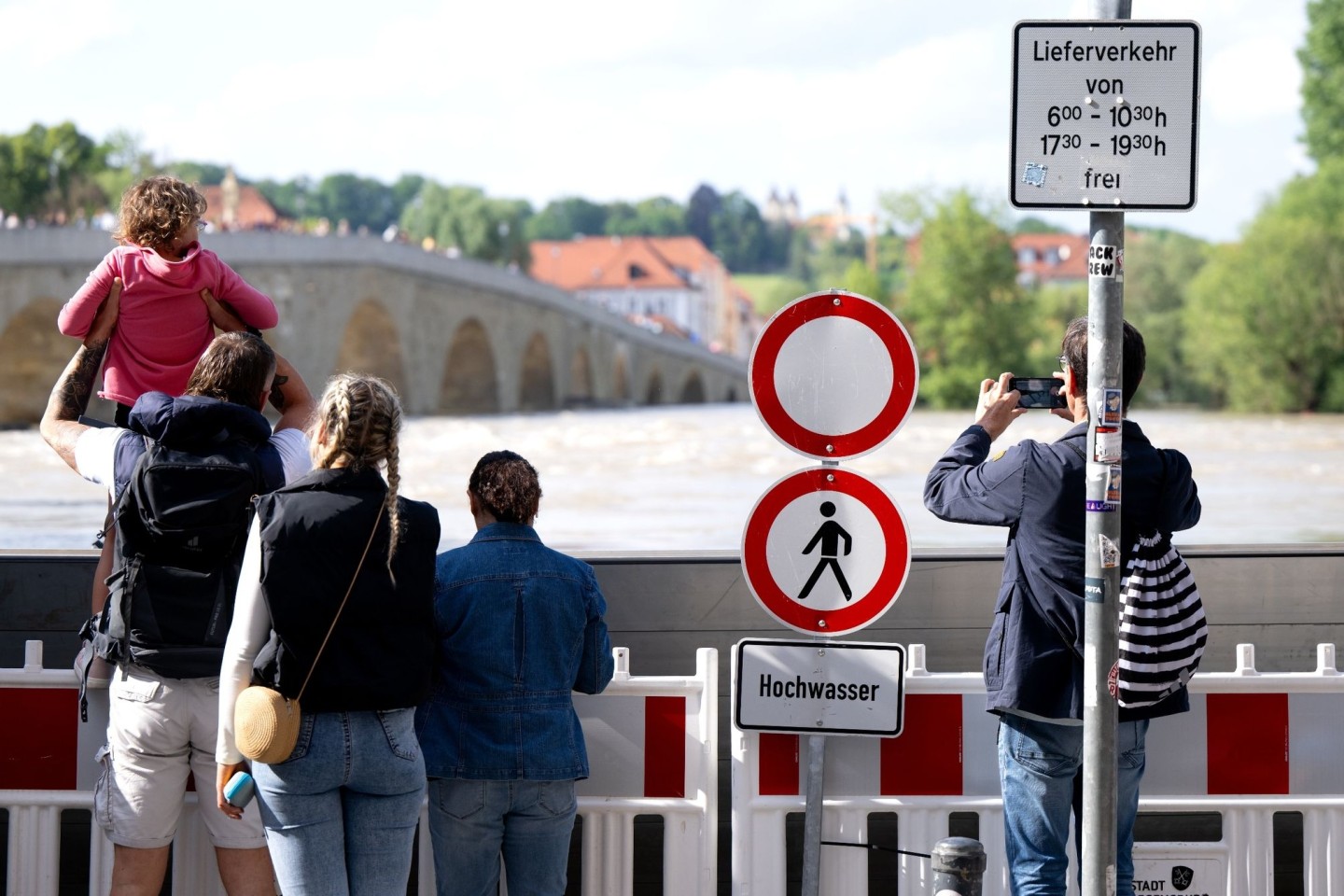 Menschen schauen sich in der Altstadt am Donauufer hinter einer Schutzwand das Hochwasser an.