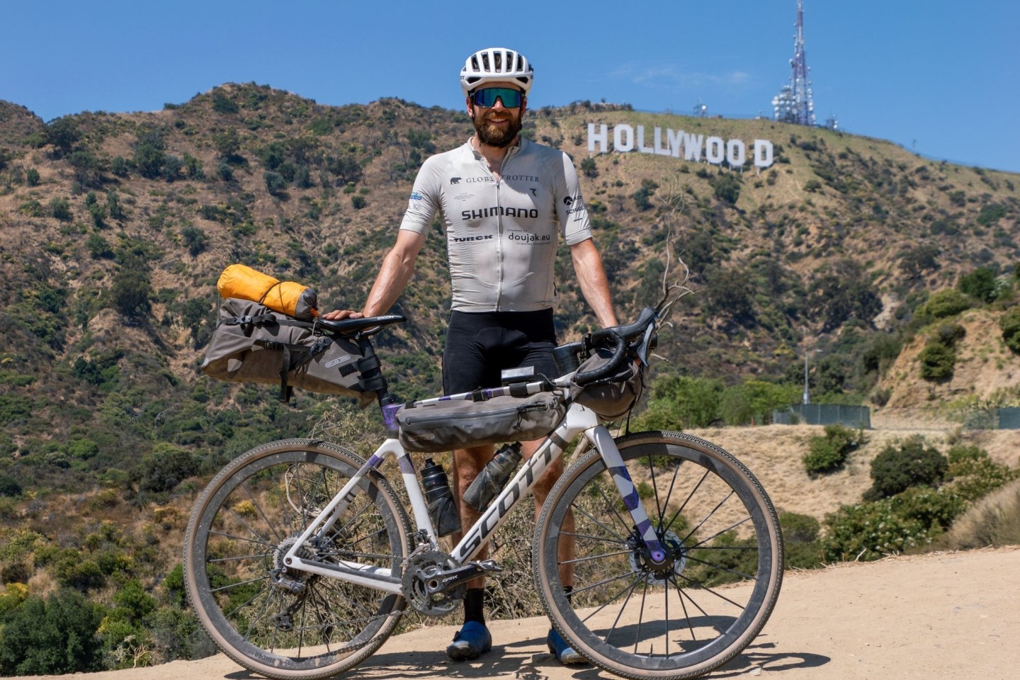 Der deutsche Athlet Jonas Deichmann mit seinem Fahrrad vor der Kulisse der Hollywood Hills in den USA.