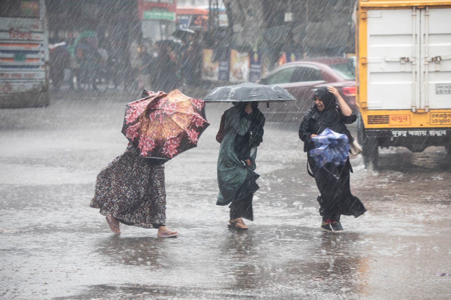 Frauen gehen bei Regen über eine Straße in Bangladesch.