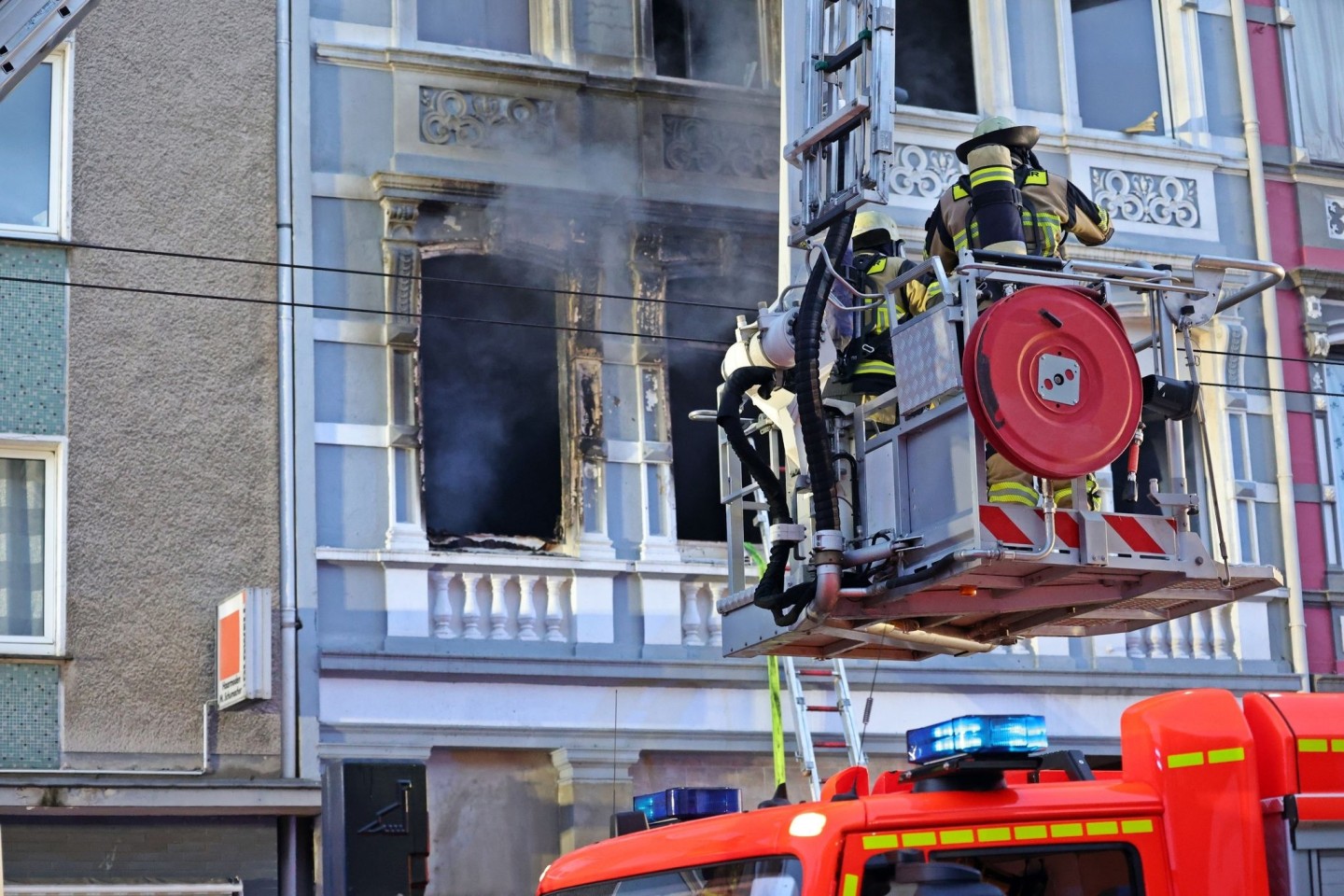 Feuerwehrmänner stehen vor dem Mehrfamilienhaus in Solingen; Rauch dringt aus einem der Fenster.