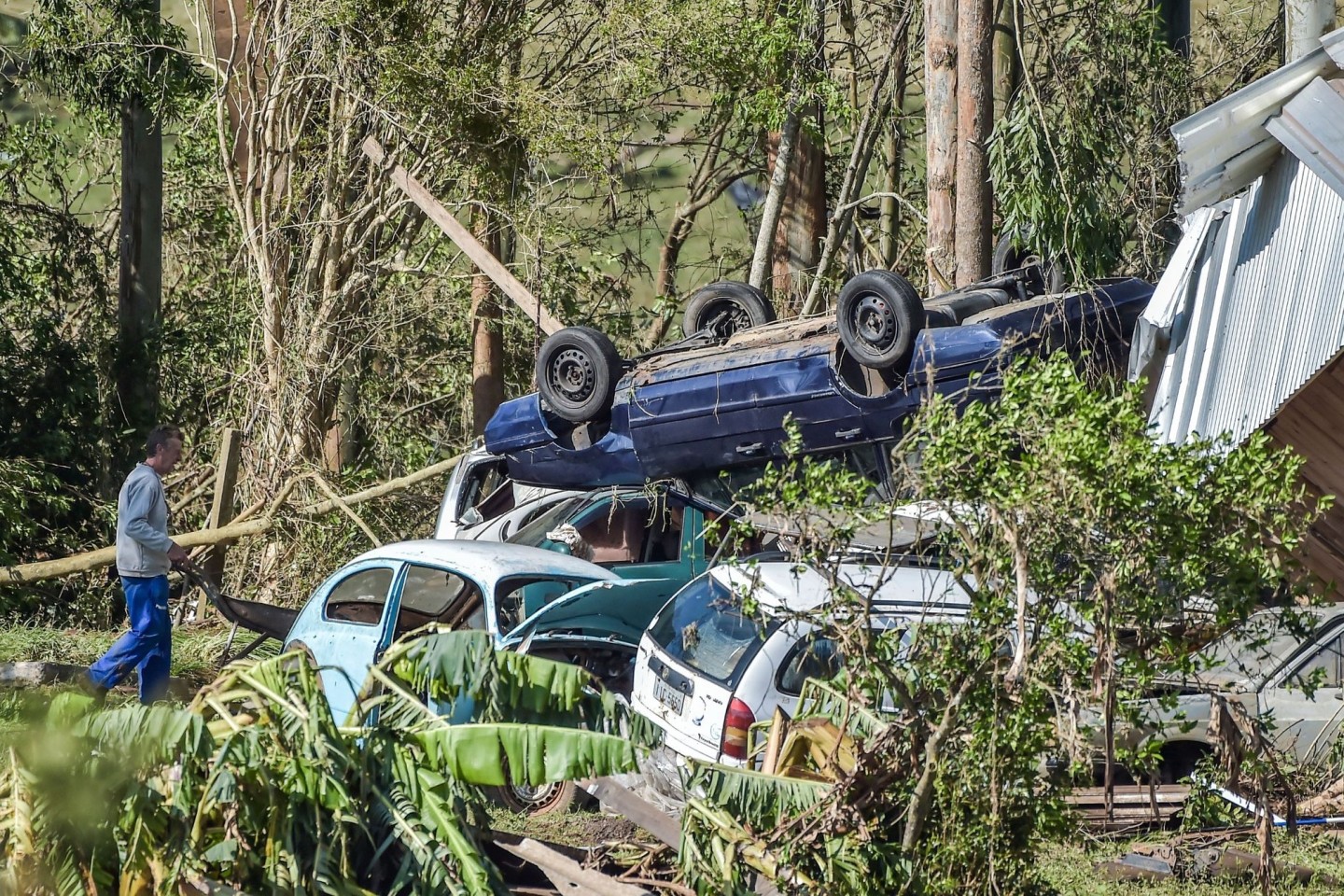 Ein Mann schiebt nach Überschwemmungen eine Schubkarre an zerstörten Autos vorbei.